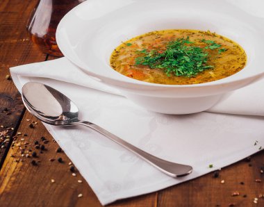 Kırsal ahşap masada servis edilen sebzeli tavuk çorbası, kaşık ve peçeteyle.