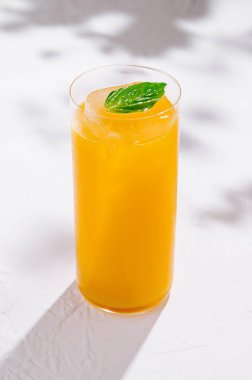 Uzun, ferahlatıcı bir portakal suyu yeşil yapraklı bir masa üzerinde duruyor.