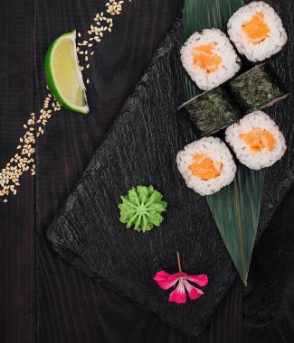 Zencefil, wasabi, limon ve susam tohumlu siyah taş tabakta servis edilen taze somon suşi rulosu.