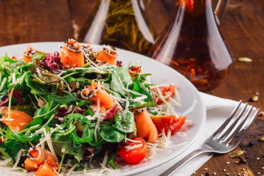 Ahşap masada servis edilen roka, somon, domates ve parmesan peynirli taze salata.