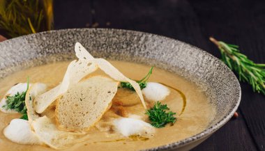 Koyu ahşap arka planda ekmek cipsi ve otlarla servis edilen lezzetli kremalı çorba.