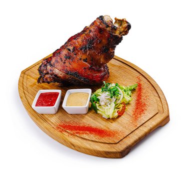 Ahşap tahtada servis edilen sulu kızarmış domuz budu soslu ve beyaz arka planda salata.