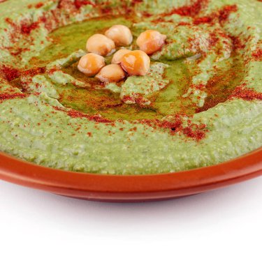 Üzerinde kırmızı biber ve zeytinyağı olan yeşil bezelye humusu.