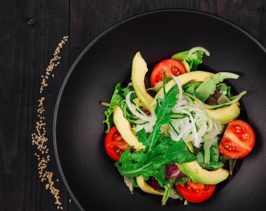 Avokadolu taze salata, domates, roka ve siyah tabakta siyah ahşap arka planda marul.