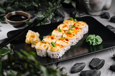 Soya sosu, turşu ve wasabi ile servis edilen siyah tabakta peynirli fırında suşi ruloları.