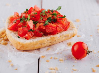 Doğranmış domates ve fesleğenle kaplanmış taze bruschetta beyaz ahşap bir masada beyaz bir kağıt parçasının üzerinde duruyor.