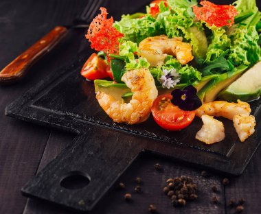 Siyah tahta masada karides, avokado ve kiraz domatesli taze salata servis edilir.