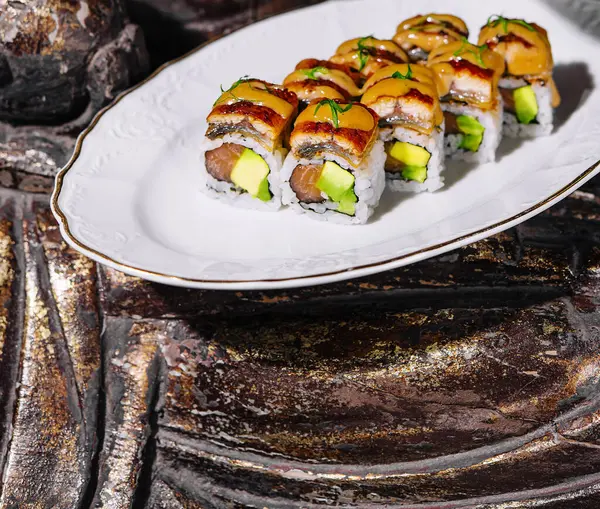 stock image Exquisite unagi sushi with avocado served on a white plate against a textured stone backdrop