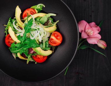 Avokado, domates ve salatalıklı vejetaryen salatası ahşap bir masada siyah bir tabakta servis edilir.