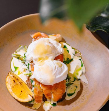 Sağlıklı ve besleyici bir kahvaltı için kızarmış ekmeğin üzerine somon ve sos ile lezzetli haşlanmış yumurta servis edilir.