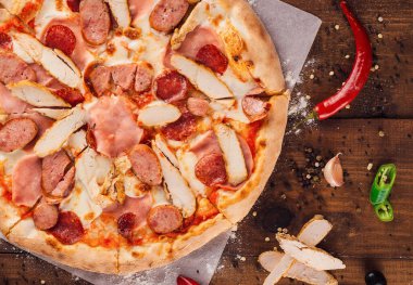 Lezzetli, yeni pişmiş, jambonlu ve tavuk filetosu dilimlenmiş, ahşap kırsal masada pizza malzemeleriyle birlikte.