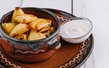 Küçük fırınlanmış turtalar beyaz ahşap bir masada beyaz soslu seramik bir kasede servis edilir.