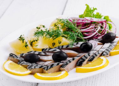 Lezzetli dilimlenmiş tuzlu uskumru haşlanmış patates, taze soğan, limon dilimleri ve beyaz tabakta servis edilen zeytinler.