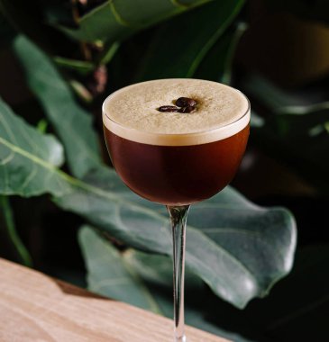 Espresso martini kokteyli, arka planda tropikal bitkiler olan bir barda duruyor.