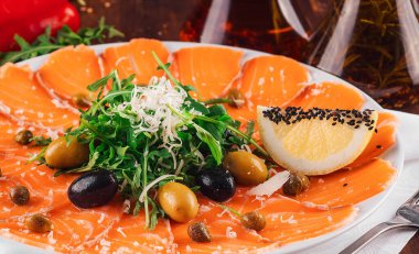 Taze roka, zeytin, limon ve ahşap restoran masasında servis edilen kapari ile süslenmiş somon carpaccio aperatifi.