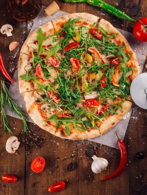 Taze pişmiş roka, kiraz domatesli ve mantarlı pizza kırsal ahşap bir masada malzemelerle çevrili.