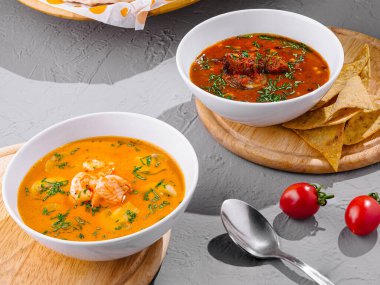Modern bir restoran masasında, bir sepet tortilla cipsinin yanında taze otlarla süslenmiş iki kase lezzetli çorba servis edilir.