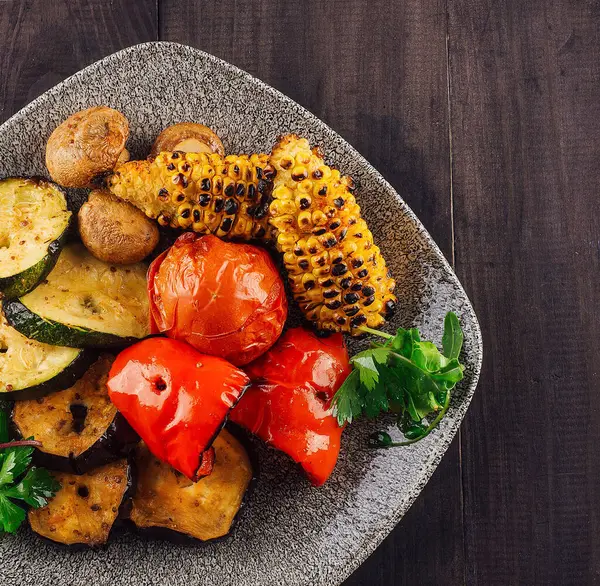 Tabakta ızgara sebzeler, ahşap masada sağlıklı yemekler servis ediliyor.