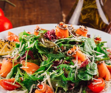 Ahşap masada servis edilen roka, somon, domates ve parmesan peynirli taze salata.