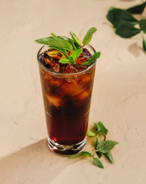 Taze nane yapraklarıyla süslenmiş ferahlatıcı koyu bir kokteyl ile dolu uzun cam bir masanın üzerinde duruyor.