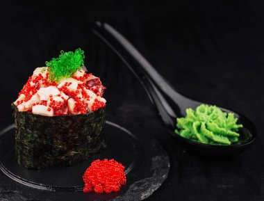 Üstü tobiko ve kırmızı havyarla kaplı Gunkan maki suşisi, wasabi ve pembe çiçekle birlikte bir tabakta sunuluyor.