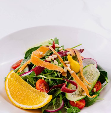 Arugula salatası, portakal dilimleri, domates, çam fıstığı, havuç ve beyaz mermer üzerinde salatalık.