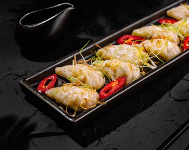 Savory steamed dumplings garnished with chili, served with soy dipping sauce