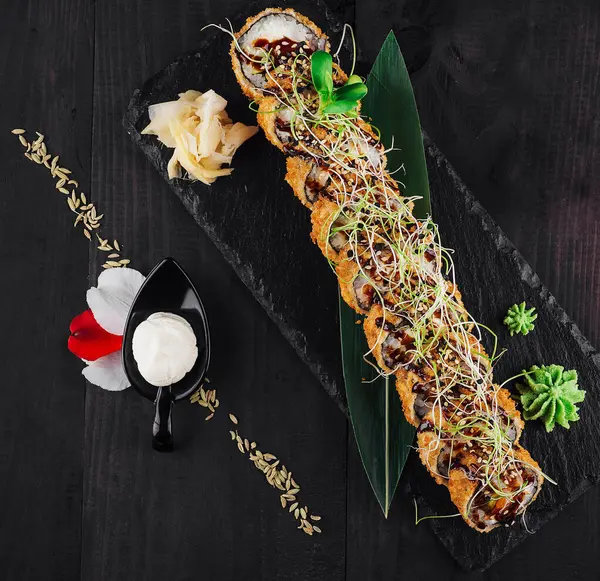 Taze tempura maki suşi rulosu çiçeklerle ve susam tohumlarıyla süslenmiş siyah bir tabakta yatıyor.