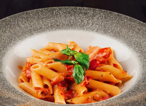 Stock image Penne pasta covered in a rich tomato sauce and garnished with fresh basil leaves