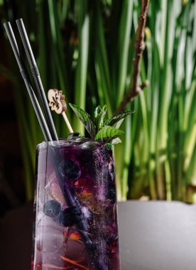 Refreshing purple cocktail with blueberries and mint stands on a bar, with vibrant plants adding a touch of nature to the background clipart