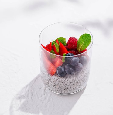 Beyaz zemin üzerinde taze ahududu, yaban mersini, çilek ve nane yapraklı Chia tohumu pudingi.