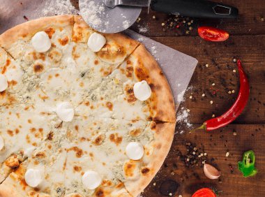 Lezzetli dört peynirli pizza, mozzarella, parmesan peyniri, gorgonzola ve ricotta ahşap masanın üzerinde, malzemelerle çevrili.