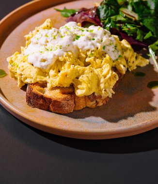 Ekşi kremalı çırpılmış yumurta ve kızarmış ekmeğin üzerinde oturan otlar sağlıklı bir kahvaltı ya da brunch için taze salata ile servis edilir.