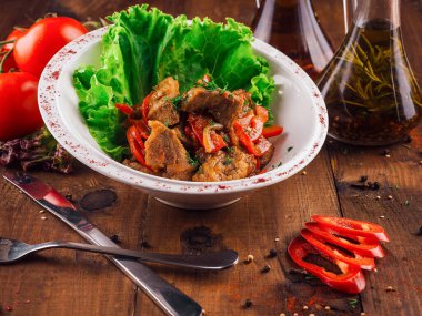 Beyaz tabakta domates ve soğandan yapılmış ve marulla süslenmiş sığır eti güveci var.