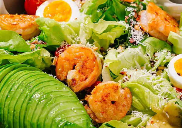 Karidesli taze salata, avokado, yumurta ve parmesan peyniri ahşap masada bir şef tarafından hazırlanıyor.