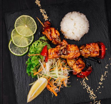 Susam tohumlu ızgara somon şişi. Beyaz pirinç, salata ve limon dilimleriyle dolu bir tabakta dinleniyor.