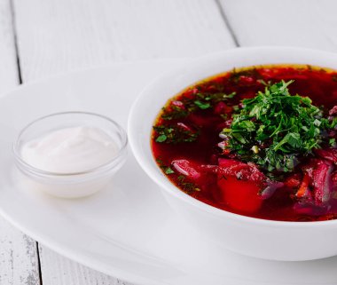 Beyaz ahşap arka planda ekşi krema ve maydanozlu geleneksel pancar çorbası çorbası.