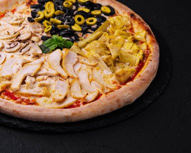 Dört farklı malzemeden oluşan bir gurme pizzanın yakın çekimi, koyu bir levha yüzeyinde servis ediliyor.