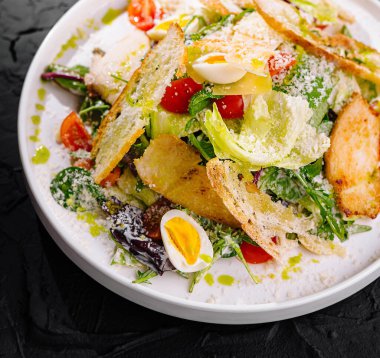 Beyaz tabakta kıtır ekmekli sezar salatası, parmesan peyniri ve yumurta.