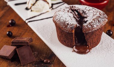 Beyaz bir tabağa erimiş çikolata damlatan çikolatalı pasta, bir kepçe vanilyalı dondurma, böğürtlen ve çikolata ile servis edilir.