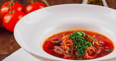 Beyaz kase lezzetli kırmızı borş ile doludur, taze otlarla süslenir ve çavdar ekmeğinin yanında servis edilir.