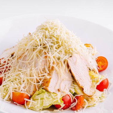 Tavuk göğsü, marul, kızarmış ekmek, vişneli domates ve beyaz arka planda parmesan peynirli Sezar salatası.