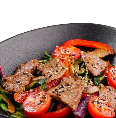 Susam tohumlu biftek ve sebzeli sıcak salata, siyah bir tabakta servis edilir, beyaz arka planda izole edilir.