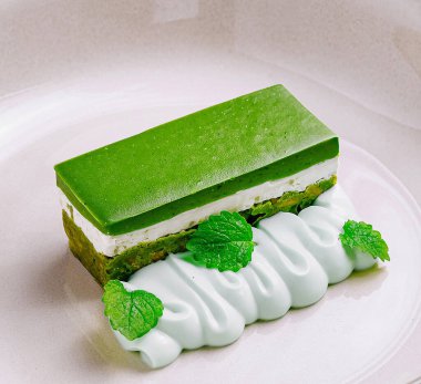 Krem peynirli kibrit yeşil çay keki ve nane yaprağı ve beyaz tabakta kremayla süslenmiş fıstık ezmesi.