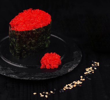 Gunkan maki sushi ve kırmızı tobiko roe siyah tahtada servis edilir.