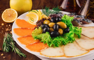 Delicious sliced cold smoked fish platter with salmon and butterfish decorated with greens and olives on white plate clipart