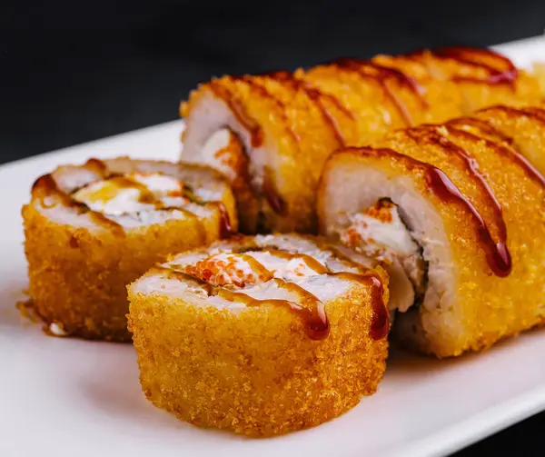 Modern bir restoranda beyaz tabakta servis edilen nefis tempura maki suşi ruloları.