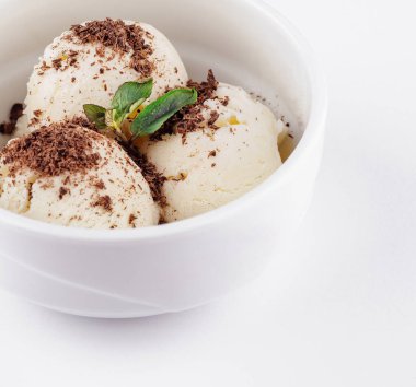 Üç kepçe vanilyalı dondurma üzerine çikolata parçacıkları ve beyaz bir kasede servis edilen nane filizi.