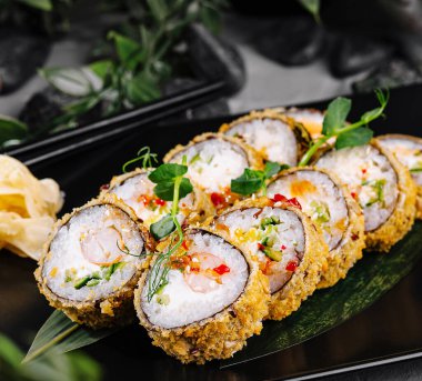 Soya soslu ve wasabi soslu taze otlarla süslenmiş çıtır tempura suşi rulosu.