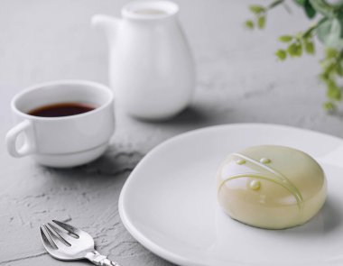 Delicate glazed dessert on a white plate with a cup of tea and teapot, minimalist setup